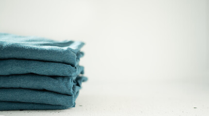 A stack of t-shirts of the same color on a light background. The minimalistic concept. Space for text.