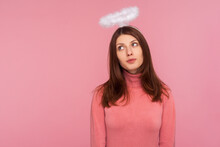 Adorable Cute Brunette Woman In Pink Sweater Standing With Halo Over Head, Angelic Innocent Expression, Faith. Indoor Studio Shot Isolated On Pink Background