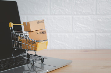 Online shopping and delivery service concept.Brown paper boxs in a shopping cart with laptop on wood table in office background.Easy shopping with finger tips for consumers.