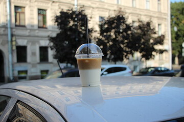 Glass of ice coffee latte on the roof of a white car on a sunny day