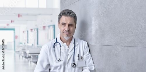 Medical portrait - Smiling doctor on hospital corridor, Trustworthy older man with gray hair.