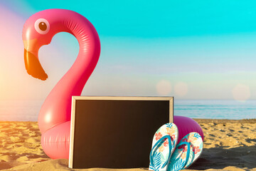 Wall Mural - Summer background. Pink inflatable flamingo with black desk, slippers for text on summer sea beach background in sunny day. Trendy summer concept.