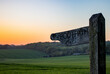 A wooden footpath sign in the english countryside at sunset with rolling green hills in the background