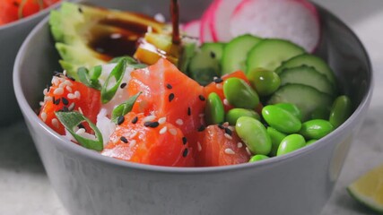 Wall Mural - Poke bowl with salmon, rice, avocado, edamame beans, cucumber and radish in gray bowl. Hawaiian ahi poke bowl, gray background.