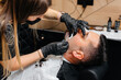 © Andrii - A professional stylist in a modern stylish barbershop shaves and cuts a young man's hair. Beauty salon, hair salon