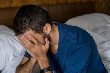 Stressed, depressed or grieving man sitting on bed covering face with hands and crying. Worried and frustrated male suffering depression or life crisis feeling desperate and helpless