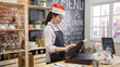 © PRPicturesProduction - beautiful girl barista in santa hat using point of sale terminal to run successful coffee store business. female waitress celebrating christmas holidays in cafe bar with xmas decor and using cash box