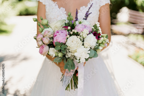 Wedding bouquet with white roses, peonies and green leaves. Bride in dress holds bouquet. Advert for wedding agency.