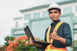 © Sawat - construction engineer has a laptop in hand and a thumbs up with the building site background