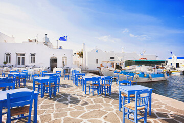 Wall Mural - Outdoor restaurant in Greece. Traditional greek cafe with beautiful street at the background. Food, travel and vacation concept. Naousa, greek fishing village on Paros island, Cyclades, Greece