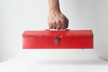 Hand holding red mechanic toolbox on white background.