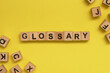 Glossary Word Written In Wooden Cube With Yellow Background