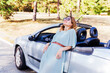 © mitarart - Outdoor fashion portrait. Attractive woman leaning and posing at convertible car. Happy pretty girl. Relaxing on summer day in nature