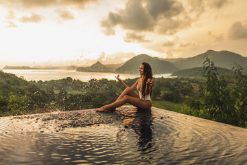 Dream journey in Asia. Woman sitting on edge luxury infinity pool an enjoying amazing mountain, rice terraces and coastline view at sunset. Inspiration travel destination.