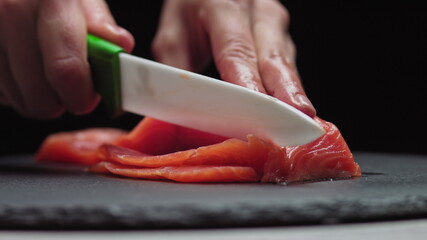 Sushi Chef Slices fresh Salmon on the sushi bar. Chef cutting salmon fillet at professional kitchen. Closeup chef hands slicing fresh fish slice in slow motion. Professional man cutting red fish