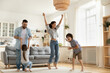 © fizkes - Happy parents with kids dancing in modern living room, having fun, playing active game, overjoyed mother and father with children siblings dancing to favorite music, jumping, celebrating event