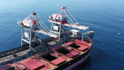 Wall Mural - Clamshell crane unloading Coal from a Cargo Ship docked at a commercial pier, Aerial view.
