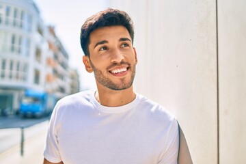 Young latin man smiling happy leaning on the wall at the city.