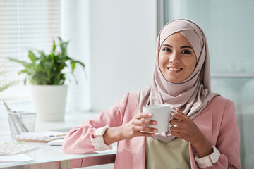 Wall Mural - Young successful Muslim businesswoman in hijab having tea or coffee at break