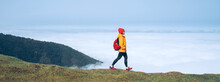 Young Female Backpacker Dressed Orange Waterproof Jacket Hiking By The Mountain Above The Cloud Route At The End Of February On Madeira Island, Portugal. Active People Around  World Traveling Concept.
