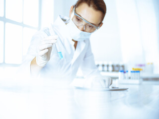 female laboratory assistant analyzing test tube with blue liquid. medicine, health care and research