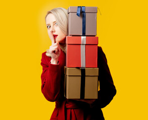 Blonde woman in red coat with gift boxes on yellow background