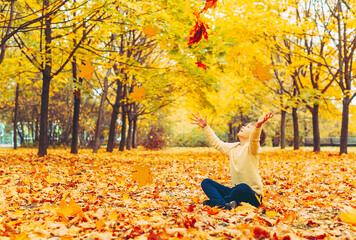 a boy sitting in an autumn park and having fun with maple trees