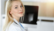 © Iryna - Woman-doctor at work while sitting at the desk in sunny clinic. Blonde cheerful physician ready to help