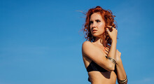 Beautiful Red Hair Woman In A Swimsuit Standing Against A Blue Sky.