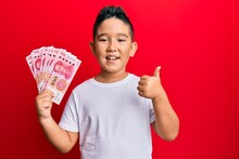 Little Boy Hispanic Kid Holding Yuan Chinese Banknotes Smiling Happy And Positive, Thumb Up Doing Excellent And Approval Sign