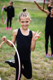 Fototapeta Tęcza - Girl gymnast training with hoop and smiling on sports playground