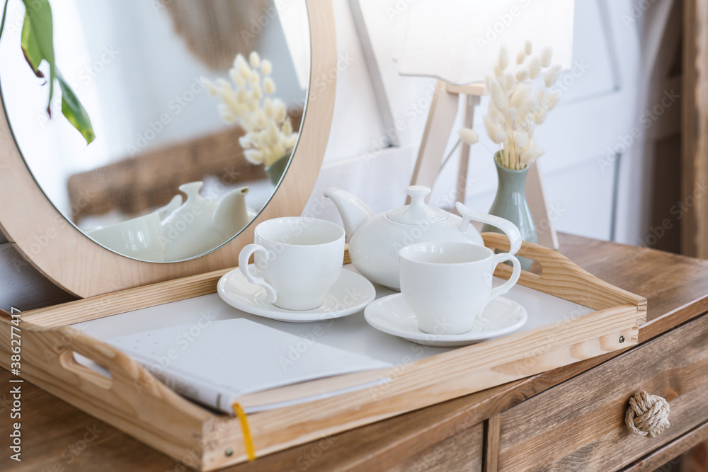 Free time at home and hot drink. Tea in kettle, cups for two on tray with notepad or book on wooden cosmetic table - obrazy, fototapety, plakaty 
