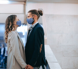 masked man and woman in love stand at a subway station.