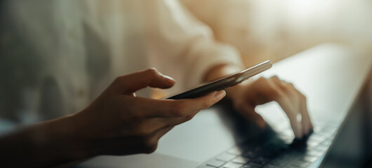 Canvas Print - Woman hand holding smartphone with laptop on the table, for your advertisement.