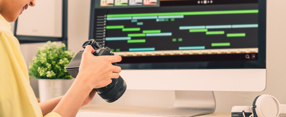 Hand holding camera and using application video editor works on the computer with footage on wooden table.