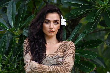 Portrait of a young woman with hair bun jasmine flower behind the ear half a turn in a flowering garden with red lips. Green nature background. Close up