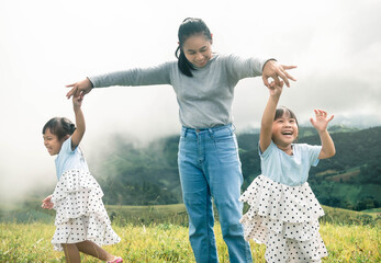 Happy young mother and two daughters playing on green lawn in the park.