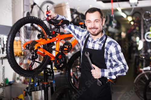 Young positive man working as mechanic for assembly of bicycles in store workshop