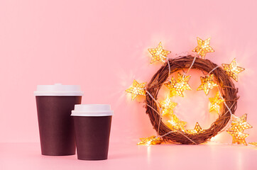 Black coffee paper cups mock up with christmas golden glowing lights  in wreath on pink background, template for advertising, design, cafe, restaurant, bar.