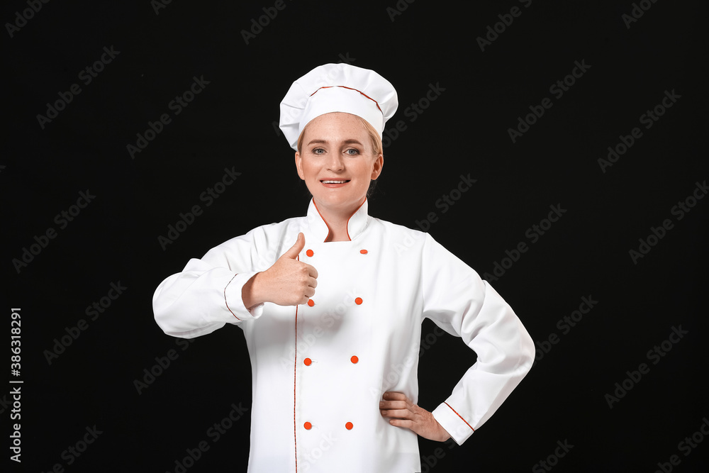 Mature female chef showing thumb-up on dark background