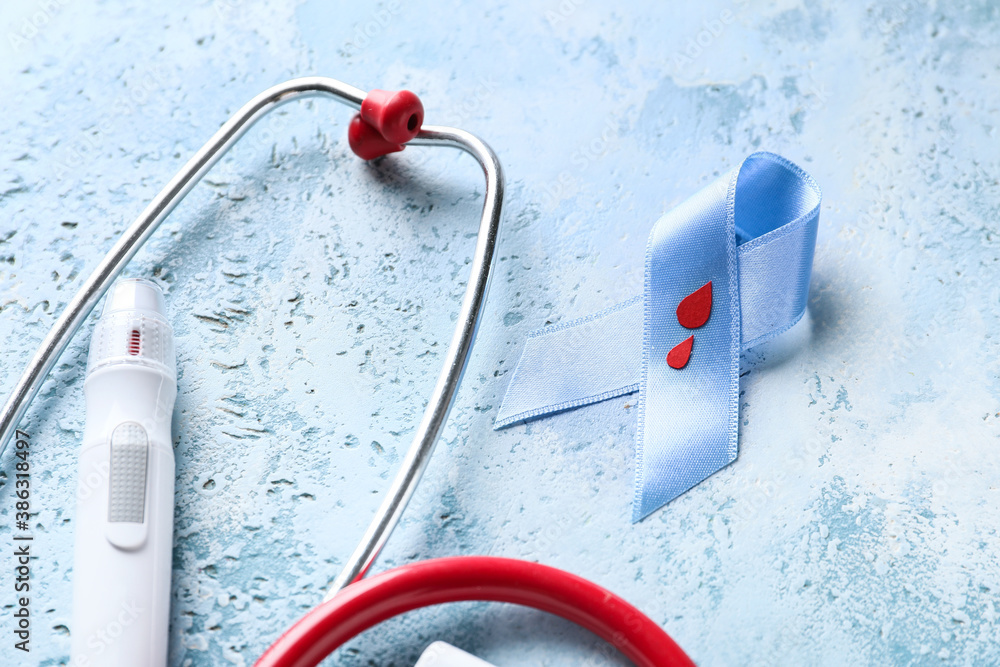 Awareness ribbon with lancet pen and stethoscope on color background. Diabetes concept