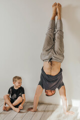 father and son go in for sports at home. The man is standing in a handstand. The boy sits and smiles. parenting, set an example. Health, sports concept.