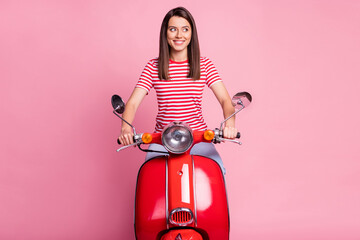 Photo portrait of curious girl sitting on red moped smiling cheerfully looking at blank space isolated on pastel pink color background