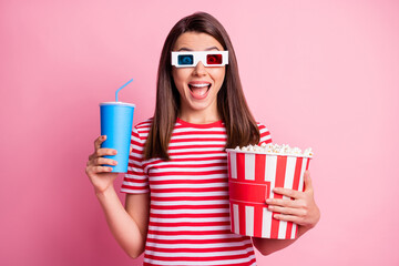 Photo portrait of surprised cheerful girl wearing 3d glasses holding pop corn cup of fizzy drink isolated on pastel pink color background