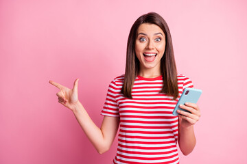 Wall Mural - Photo portrait of amazed woman keeping cellphone pointing with finger at copyspace isolated on pastel pink color background