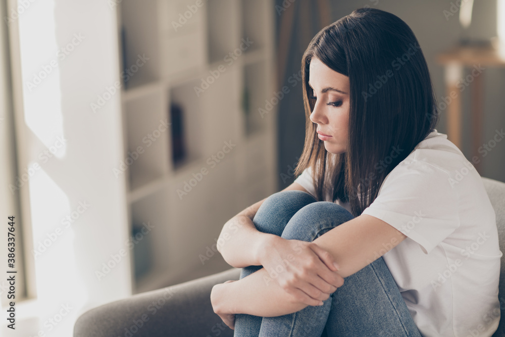 Profile side photo of attractive young girl feeling upset hug her knees sitting couch in house indoors - obrazy, fototapety, plakaty 