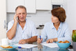 © JackF - Mature family couple sitting at kitchen table with phone signing documents together
