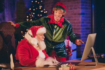 Photo portrait of elf pointing finger at desktop screen while santa claus sits surprised