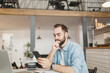 © ViDi Studio - Pensive young man sitting at table in coffee shop cafe working studying on laptop pc computer using cell phone relaxing in restaurant during free time indoor. Freelance mobile office business concept.