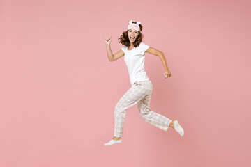 Wall Mural - Full length side view portrait of cheerful young woman 20s in white pajamas home wear jumping like running while resting at home isolated on pastel pink background studio. Relax good mood concept.